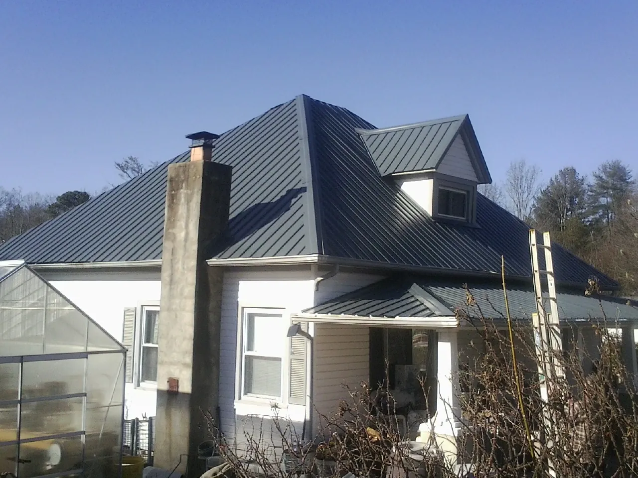 Dark blue standing seam metal roof on a white farmhouse with dormer — Slate & Tile Roof Repair by Roofing Brothers in Cottonton