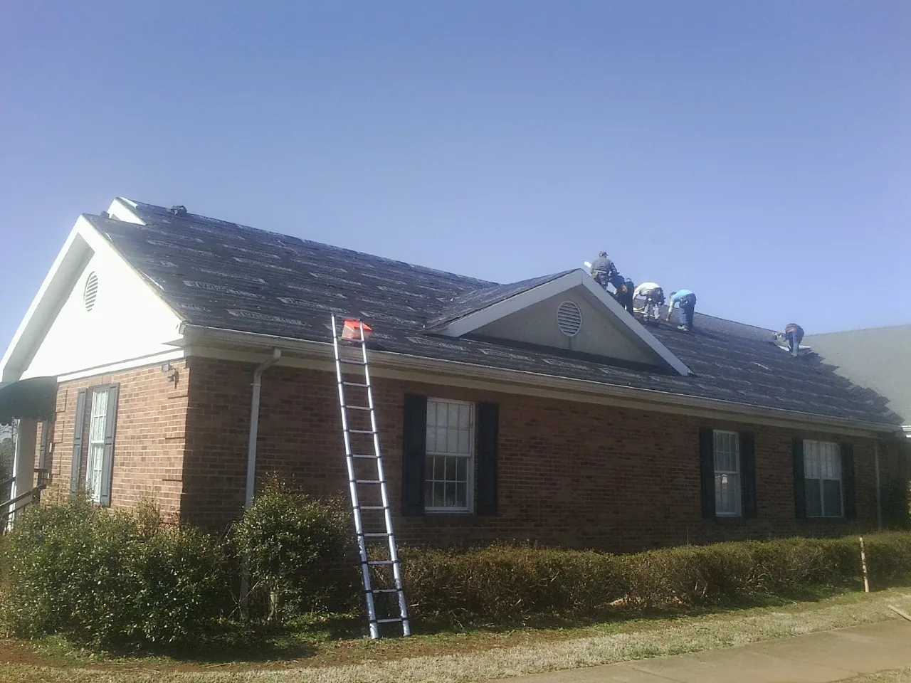 Crew tearing shingles off a brick ranch roof with a ladder set — Metal Roof Repair work by our crew in Cottonton