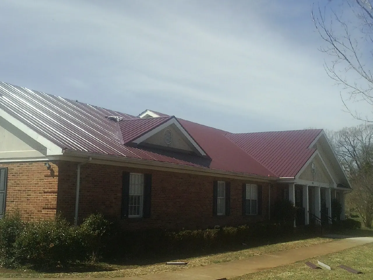 Red metal roof with gabled entries on a long brick building, from a Hail Damage Roof Repair job in Cottonton