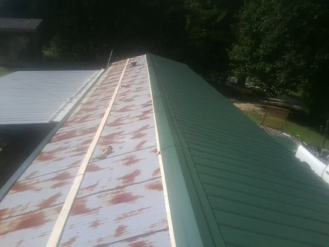 Old rusted panels beside newly installed green metal roofing — Wind Damage Roof Repair by Roofing Brothers in Cottonton