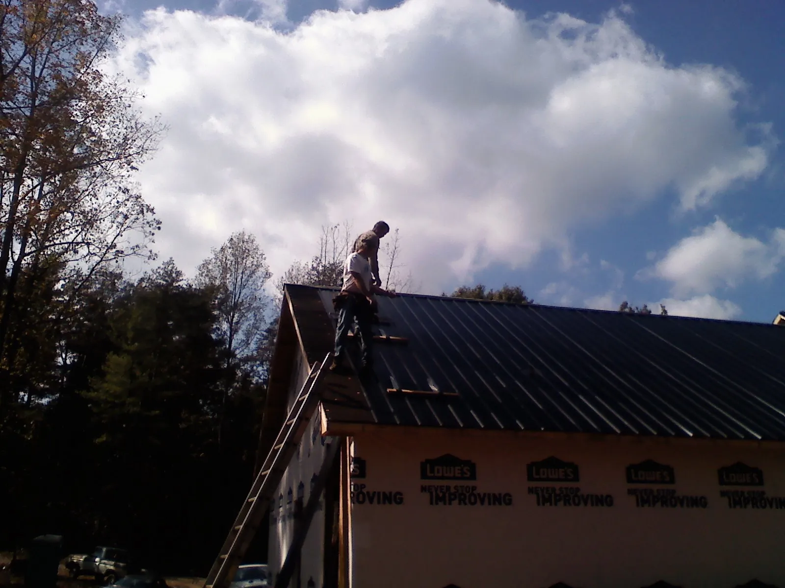 Roofer fastening dark metal panels high against a cloudy sky, from a Roof Inspection job in Cottonton