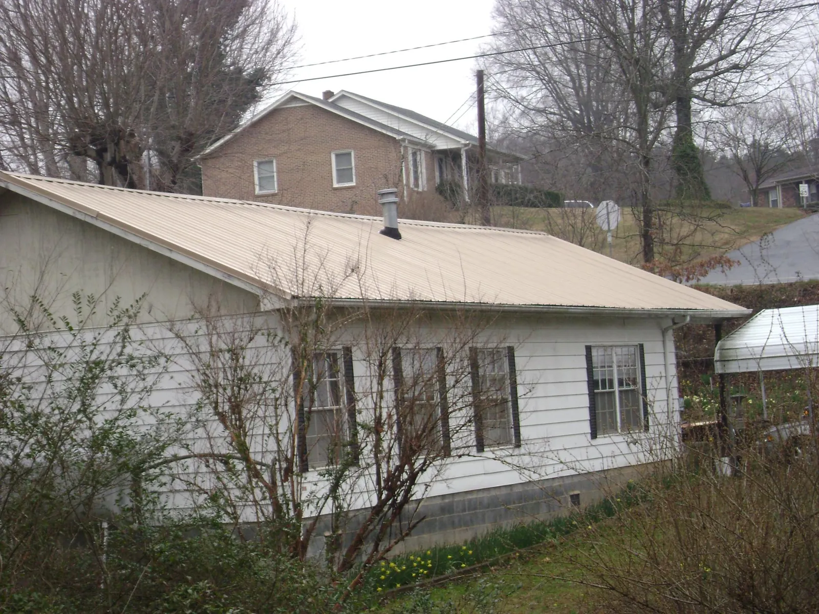 Tan metal roof on a white sided house set into a hillside — Commercial Roofing by Roofing Brothers in Cottonton
